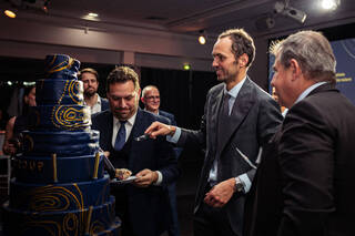 MEOGROUP employees celebrating at an event around a Group-branded cake